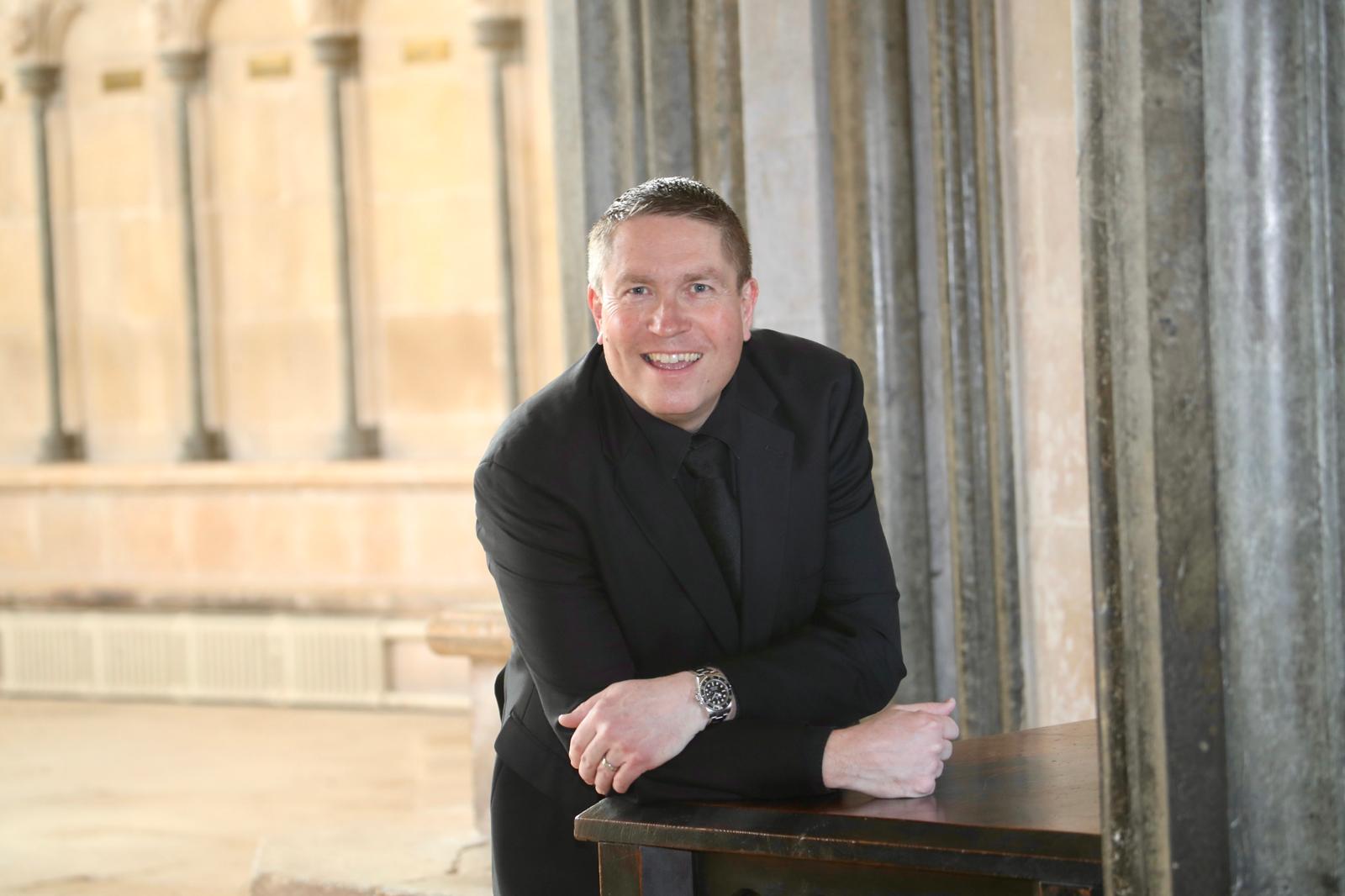 Matthew Minter leaning forward and smiling in a cloister.