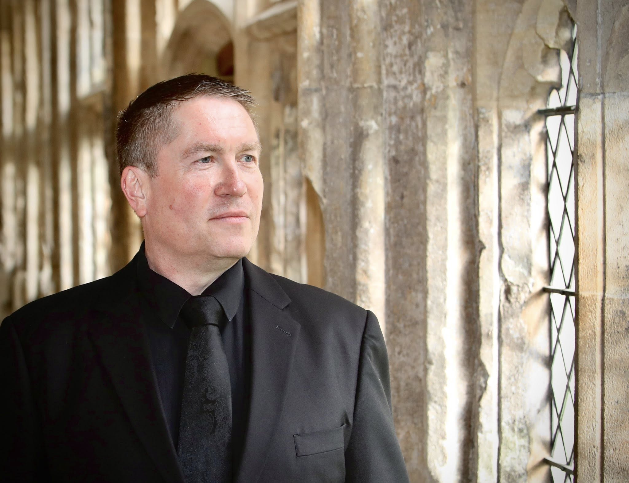 Matthew Minter standing in formal attire beside a stone window.
